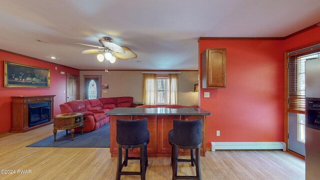 kitchen featuring ceiling fan, a baseboard radiator, a kitchen breakfast bar, light hardwood / wood-style flooring, and ornamental molding