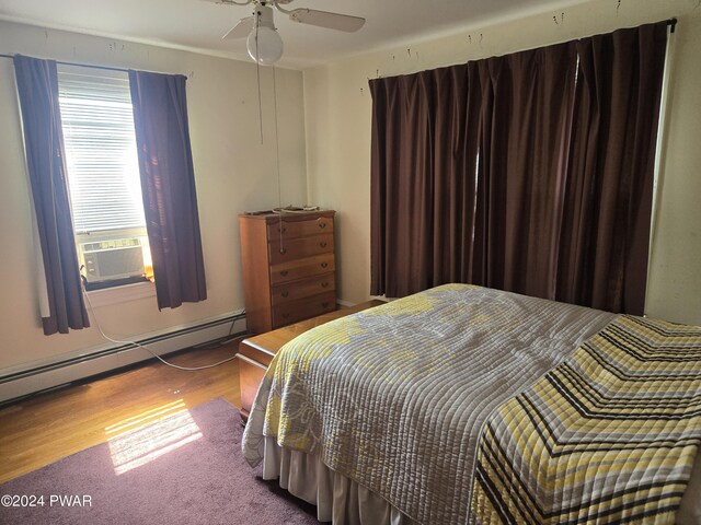 bedroom featuring ceiling fan, hardwood / wood-style floors, and a baseboard heating unit