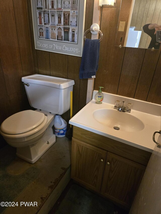 bathroom featuring vanity, wood walls, and toilet