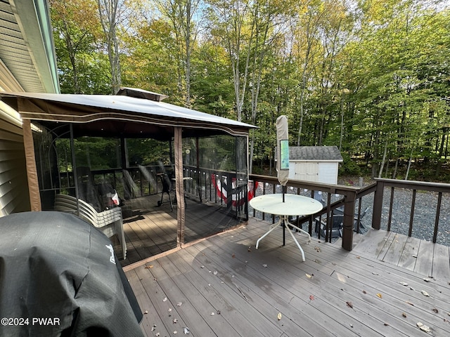 wooden deck featuring a gazebo, a storage unit, and a grill