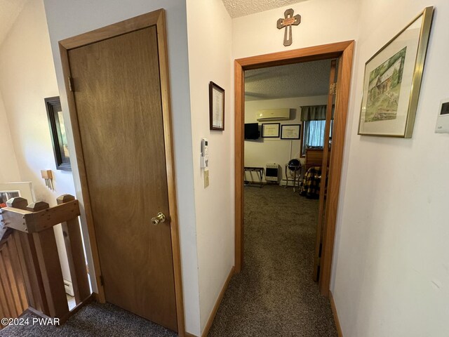 corridor with a wall mounted air conditioner, a textured ceiling, and dark carpet