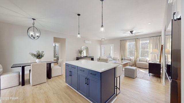 kitchen with pendant lighting, ceiling fan, a kitchen island, blue cabinets, and light wood-type flooring