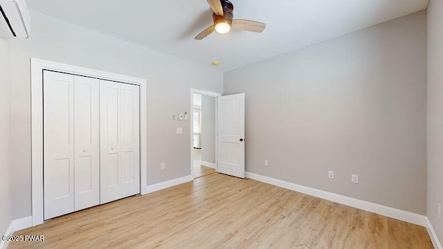 unfurnished bedroom with a wall mounted air conditioner, light hardwood / wood-style flooring, a closet, and ceiling fan