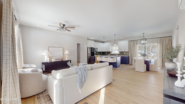 living room featuring ceiling fan with notable chandelier and light wood-type flooring