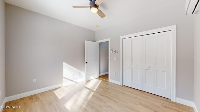 unfurnished bedroom with ceiling fan, a wall unit AC, light hardwood / wood-style floors, and a closet