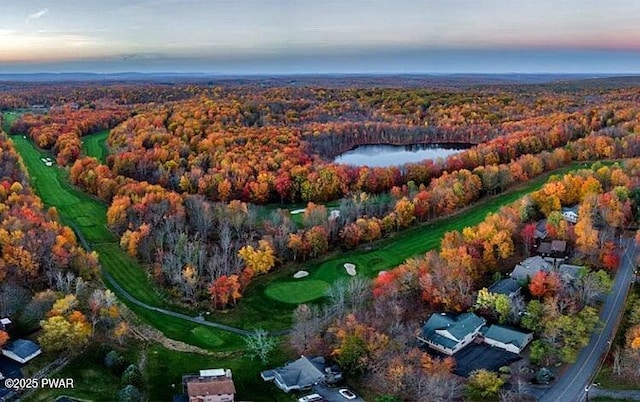 aerial view of property's location featuring a forest, a golf course, and a nearby body of water
