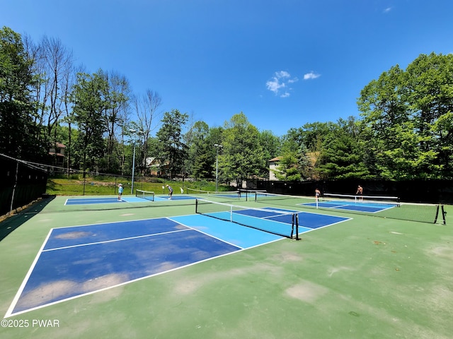 view of tennis court with community basketball court, fence, and view of scattered trees