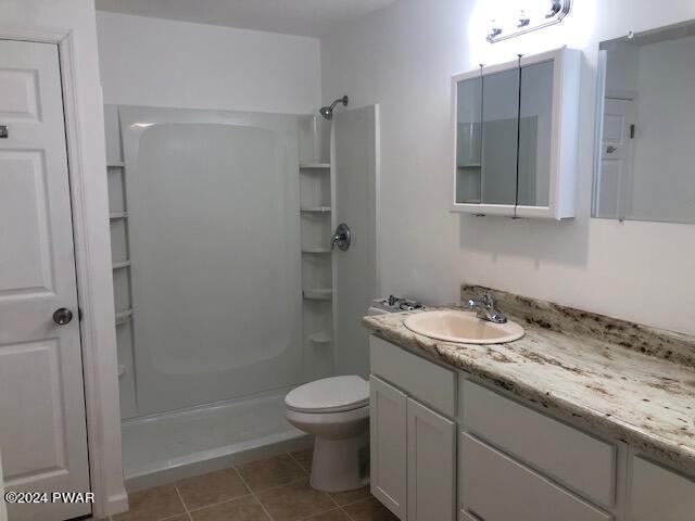 bathroom with toilet, tile patterned flooring, vanity, and walk in shower