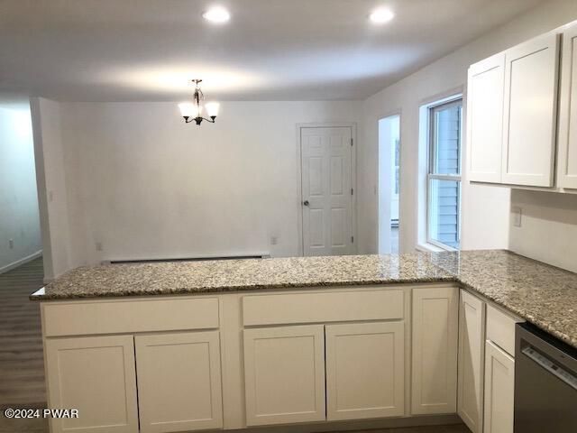 kitchen featuring kitchen peninsula, stainless steel dishwasher, light stone counters, a notable chandelier, and white cabinetry