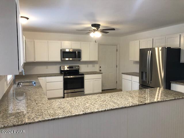 kitchen with kitchen peninsula, appliances with stainless steel finishes, light stone counters, sink, and white cabinetry