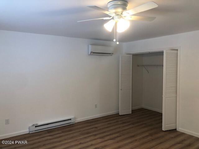 unfurnished bedroom with dark hardwood / wood-style flooring, a wall unit AC, ceiling fan, a baseboard radiator, and a closet