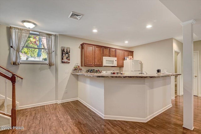 kitchen with kitchen peninsula, light stone counters, dark hardwood / wood-style flooring, and white appliances