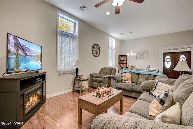 living room with ceiling fan with notable chandelier, a wealth of natural light, and light hardwood / wood-style flooring