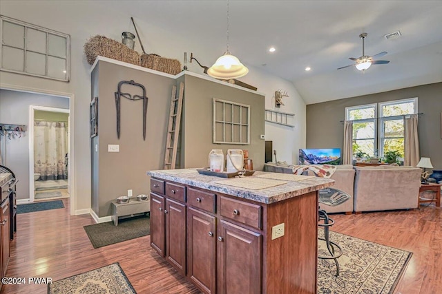 kitchen featuring a center island, hanging light fixtures, vaulted ceiling, a breakfast bar area, and light wood-type flooring