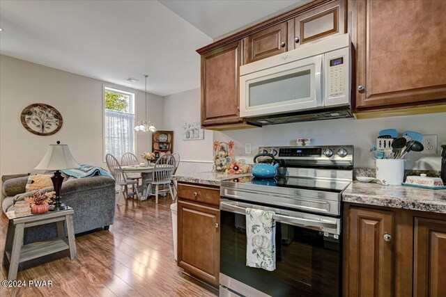 kitchen featuring light stone countertops, hanging light fixtures, a notable chandelier, hardwood / wood-style floors, and stainless steel range with electric cooktop