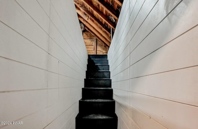 staircase featuring vaulted ceiling and wood walls