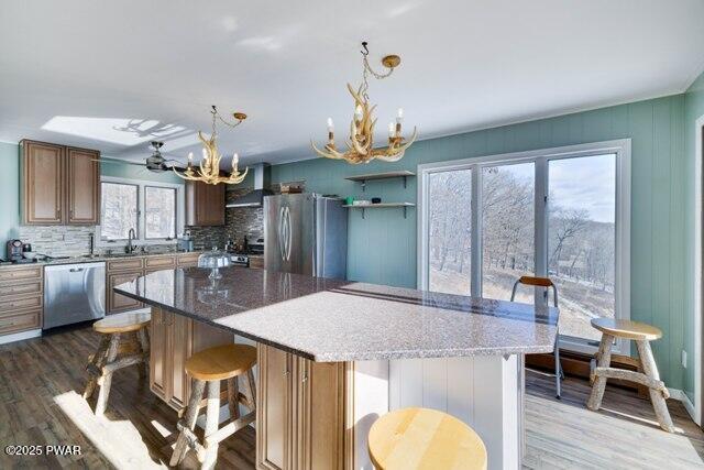 kitchen featuring an inviting chandelier, wall chimney exhaust hood, tasteful backsplash, a kitchen island, and stainless steel appliances