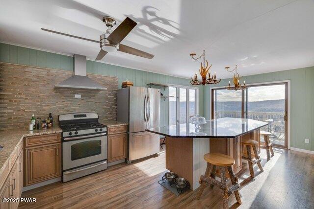 kitchen with wall chimney exhaust hood, stainless steel appliances, light hardwood / wood-style floors, a kitchen island, and a breakfast bar area