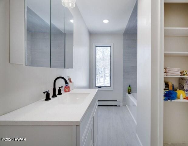 bathroom featuring a washtub, vanity, wood-type flooring, and a baseboard heating unit