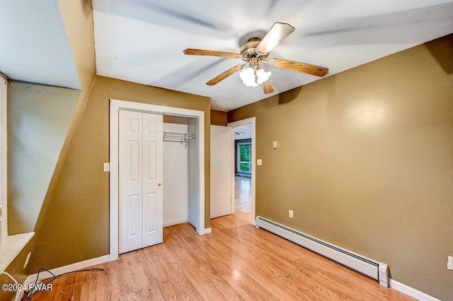 unfurnished bedroom featuring a closet, baseboard heating, light hardwood / wood-style floors, and ceiling fan