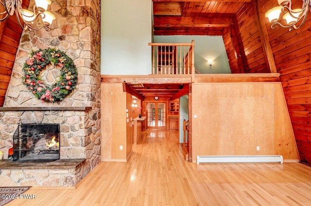 interior space with wood ceiling, baseboard heating, beamed ceiling, hardwood / wood-style floors, and a stone fireplace