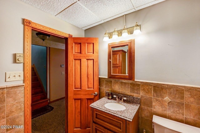 bathroom featuring a paneled ceiling, vanity, tile walls, and toilet