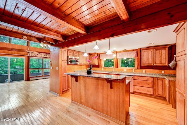 kitchen featuring a center island, light stone countertops, decorative light fixtures, beam ceiling, and stainless steel appliances