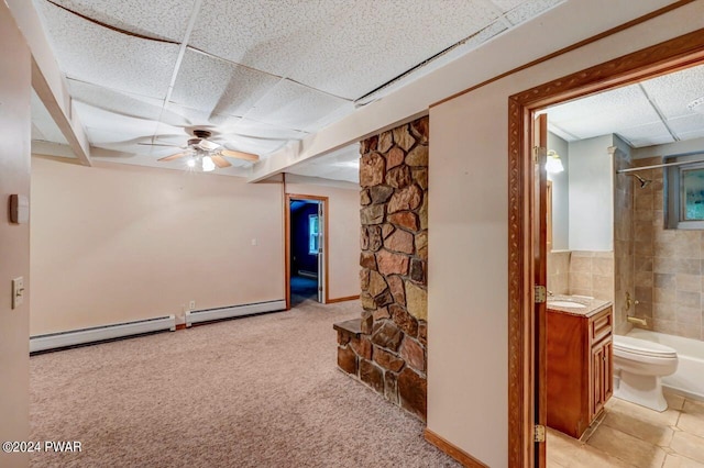 basement featuring a drop ceiling, ceiling fan, and a baseboard heating unit