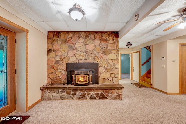 carpeted living room featuring a paneled ceiling, a wood stove, and ceiling fan