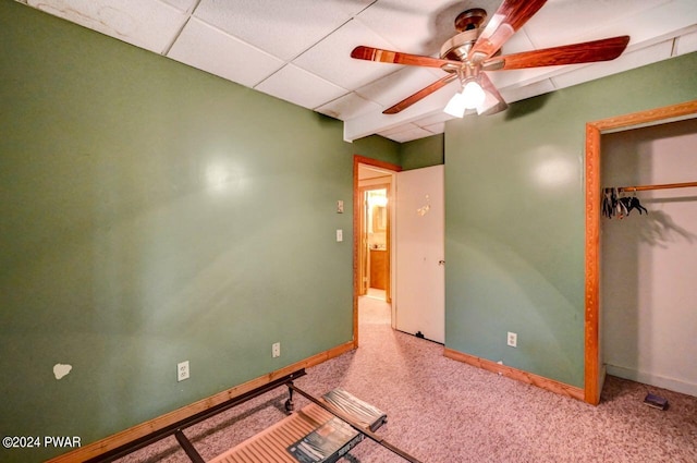 unfurnished bedroom with a closet, ceiling fan, a drop ceiling, and carpet