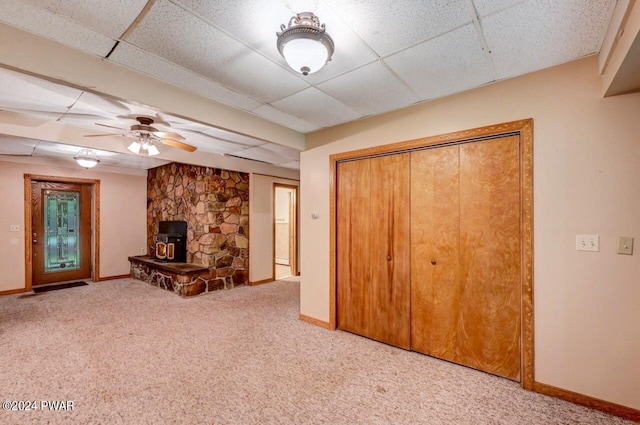 unfurnished living room featuring a paneled ceiling, carpet flooring, ceiling fan, and a wood stove