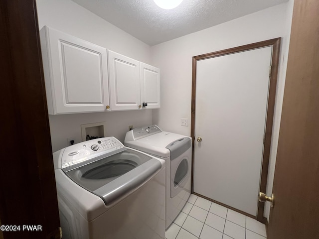 laundry room featuring cabinets, light tile patterned flooring, washing machine and dryer, and a textured ceiling