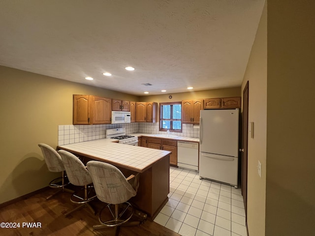 kitchen with tile counters, sink, kitchen peninsula, white appliances, and a kitchen bar