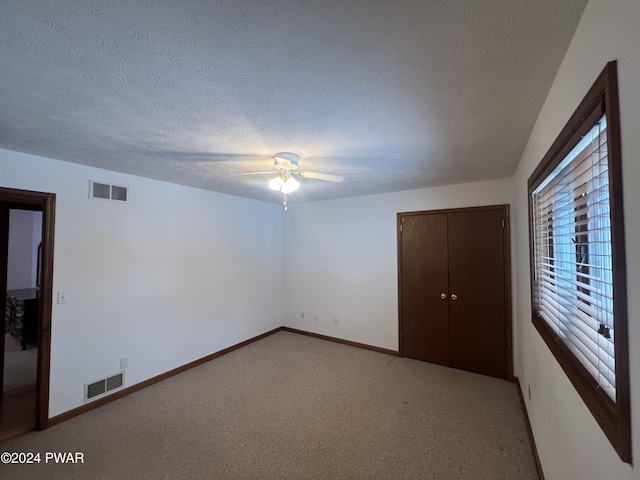 unfurnished bedroom featuring ceiling fan, a closet, light carpet, and a textured ceiling