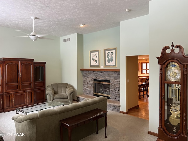 living room featuring ceiling fan, a stone fireplace, light colored carpet, and a textured ceiling