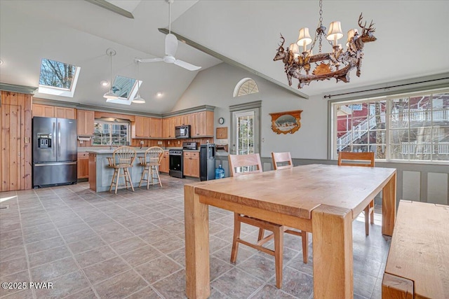 dining space featuring high vaulted ceiling, a skylight, and ceiling fan with notable chandelier