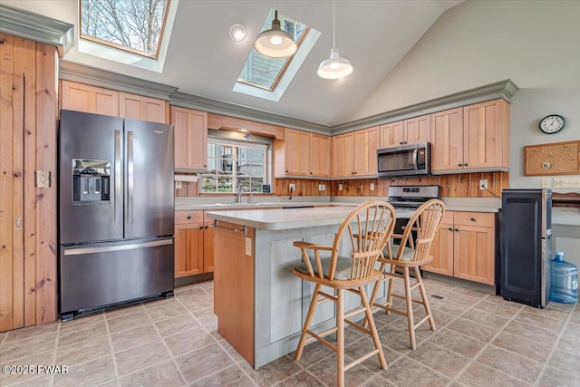 kitchen featuring stainless steel appliances, vaulted ceiling with skylight, light brown cabinetry, and light countertops