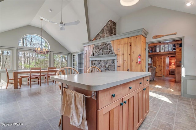 kitchen featuring high vaulted ceiling, ceiling fan with notable chandelier, decorative light fixtures, a kitchen island, and light countertops