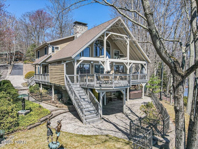 back of house with covered porch, a chimney, roof with shingles, a patio area, and stairs
