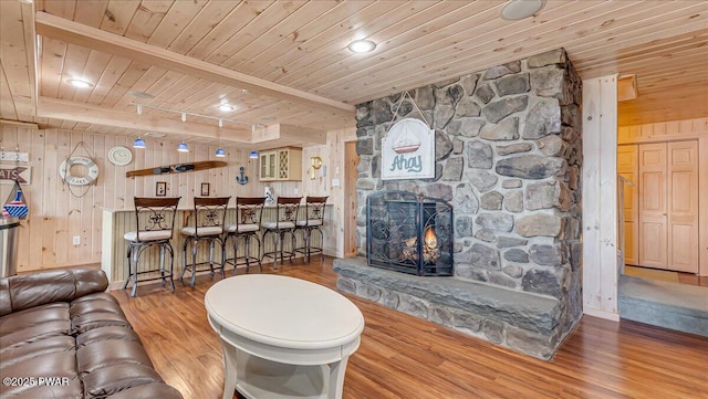 living room with a stone fireplace, wood ceiling, wood finished floors, and wooden walls
