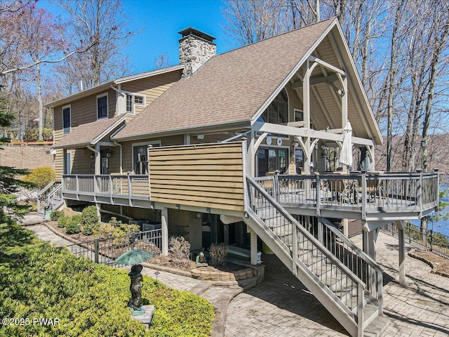 rear view of house featuring a deck, a shingled roof, stairs, and a chimney