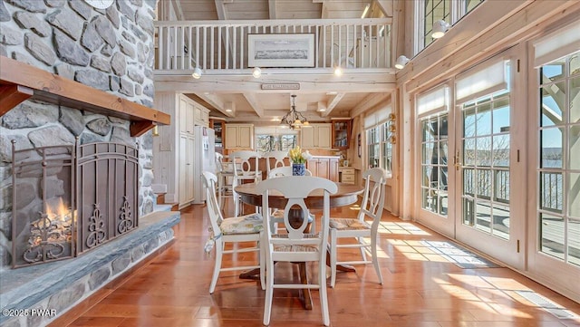 dining area featuring a stone fireplace, visible vents, beam ceiling, a chandelier, and light wood-style floors