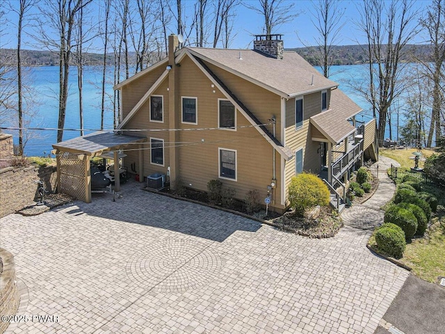 rear view of property featuring a water view, central air condition unit, and a chimney