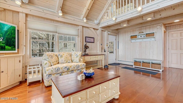 living area with wooden walls, lofted ceiling with beams, baseboard heating, wood-type flooring, and wood ceiling