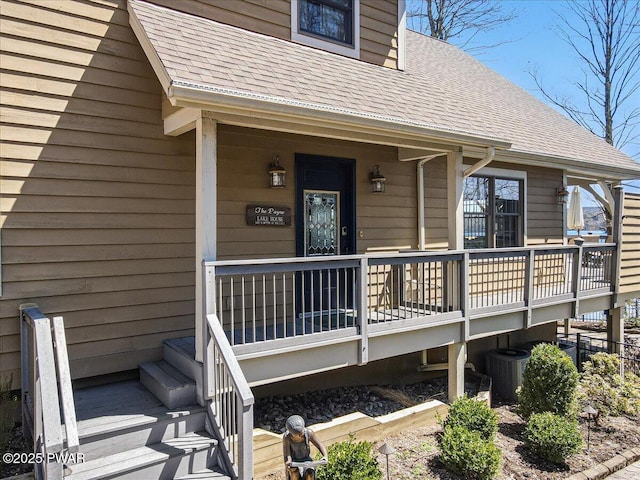 doorway to property with a shingled roof, central air condition unit, and covered porch