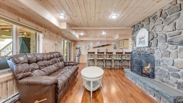 living area featuring wood walls, a stone fireplace, wooden ceiling, wood finished floors, and a baseboard heating unit
