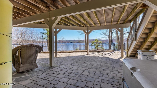 view of patio with a water view, fence, and stairs