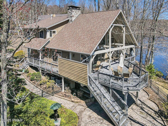 exterior space with fence, a deck, roof with shingles, a chimney, and stairway