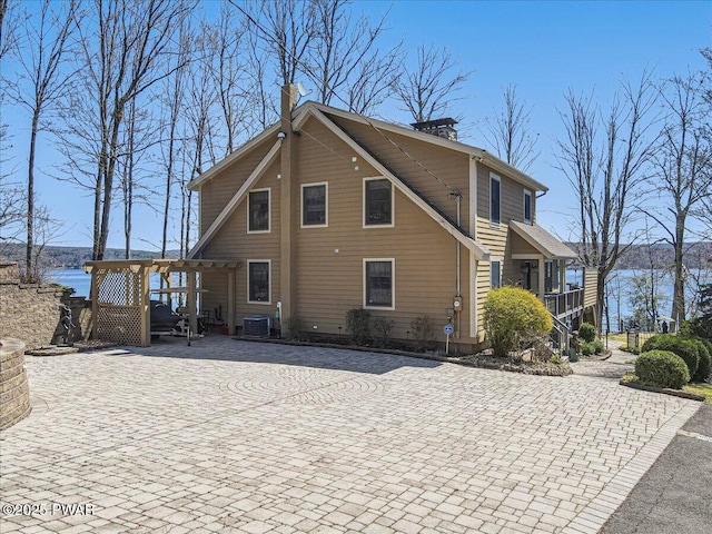 back of property with a water view, central AC, and a chimney