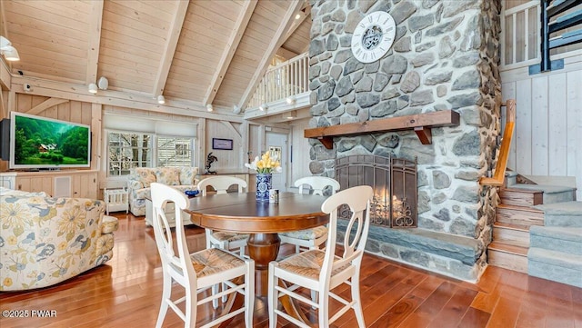 dining space featuring wood ceiling, a fireplace, beamed ceiling, wooden walls, and hardwood / wood-style floors